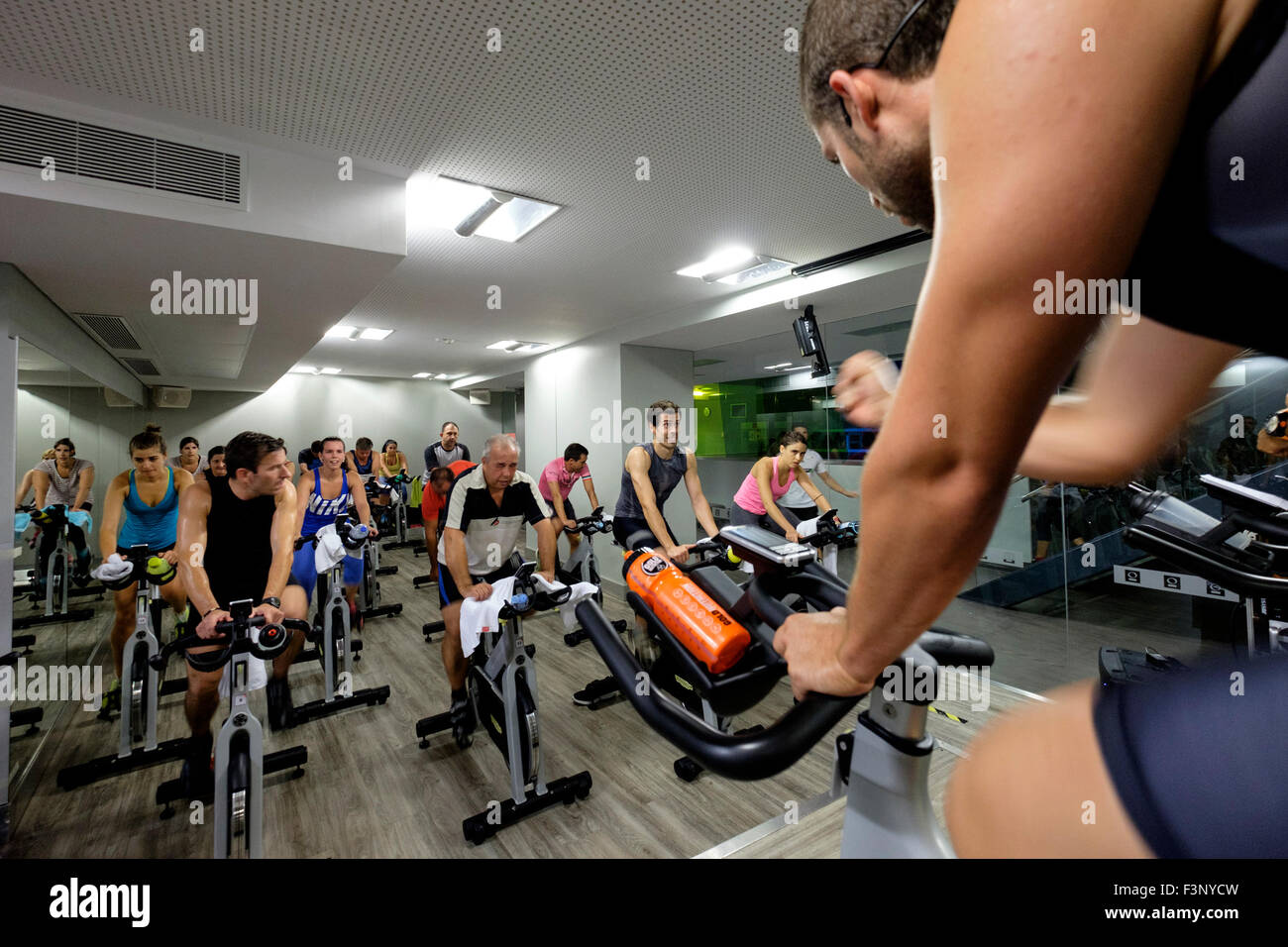 Fitness instructor encourages people riding stationary bicycles during a spinning class at the gym Stock Photo