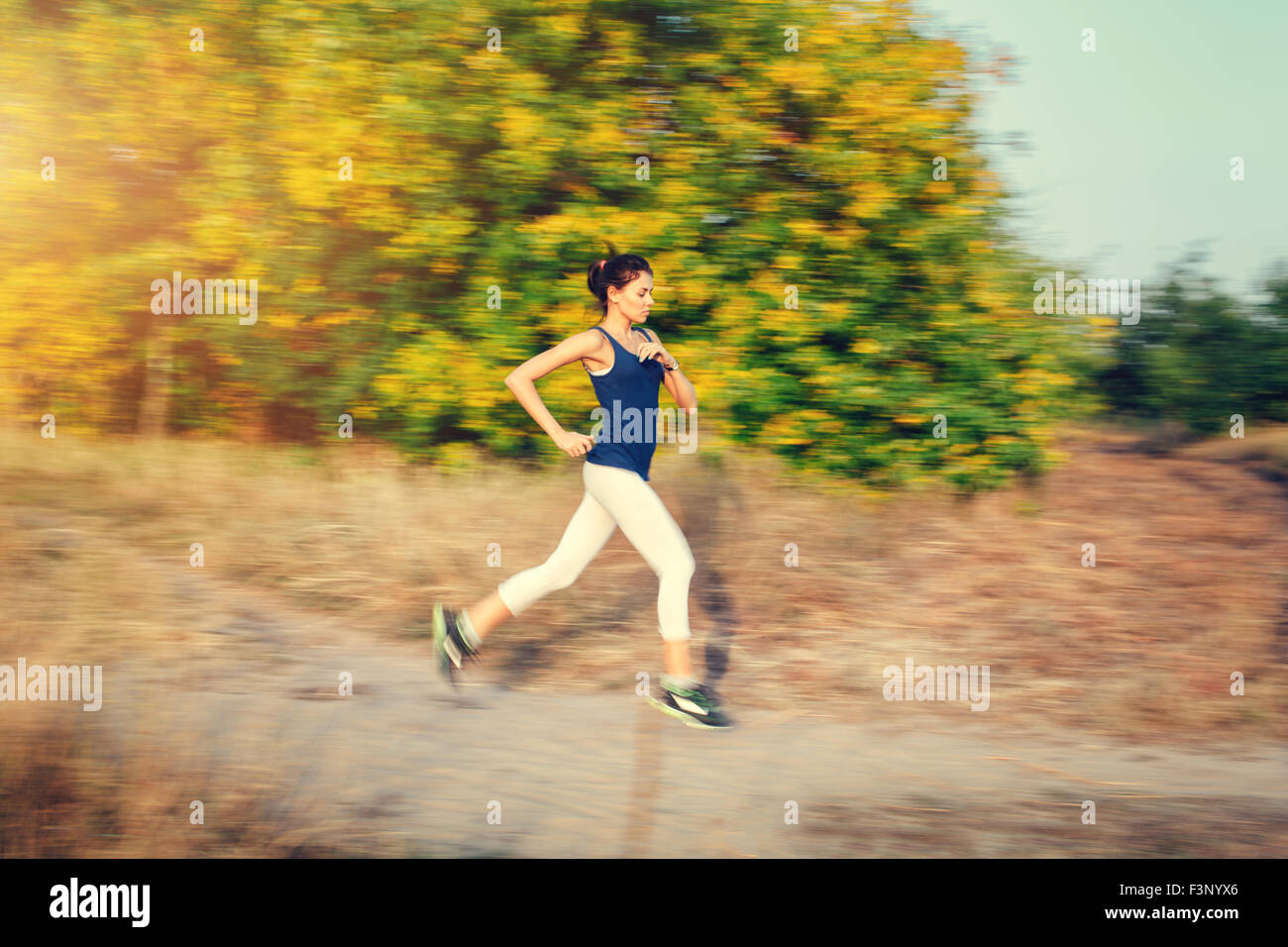Young woman running on a rural road at sunset in autumn forest. Lifestyle sports background Stock Photo