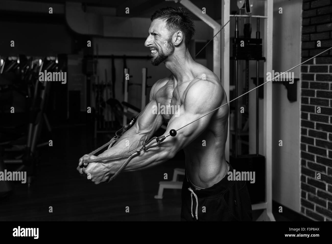 Bodybuilder Is Working On His Chest With Cable Crossover In A Dark Gym Stock Photo