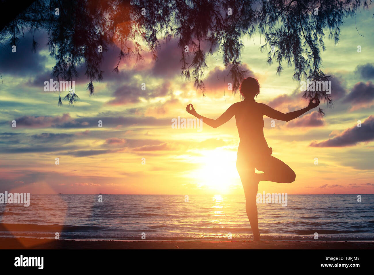 Silhouette of woman standing at yoga pose on the beach during sunset ...