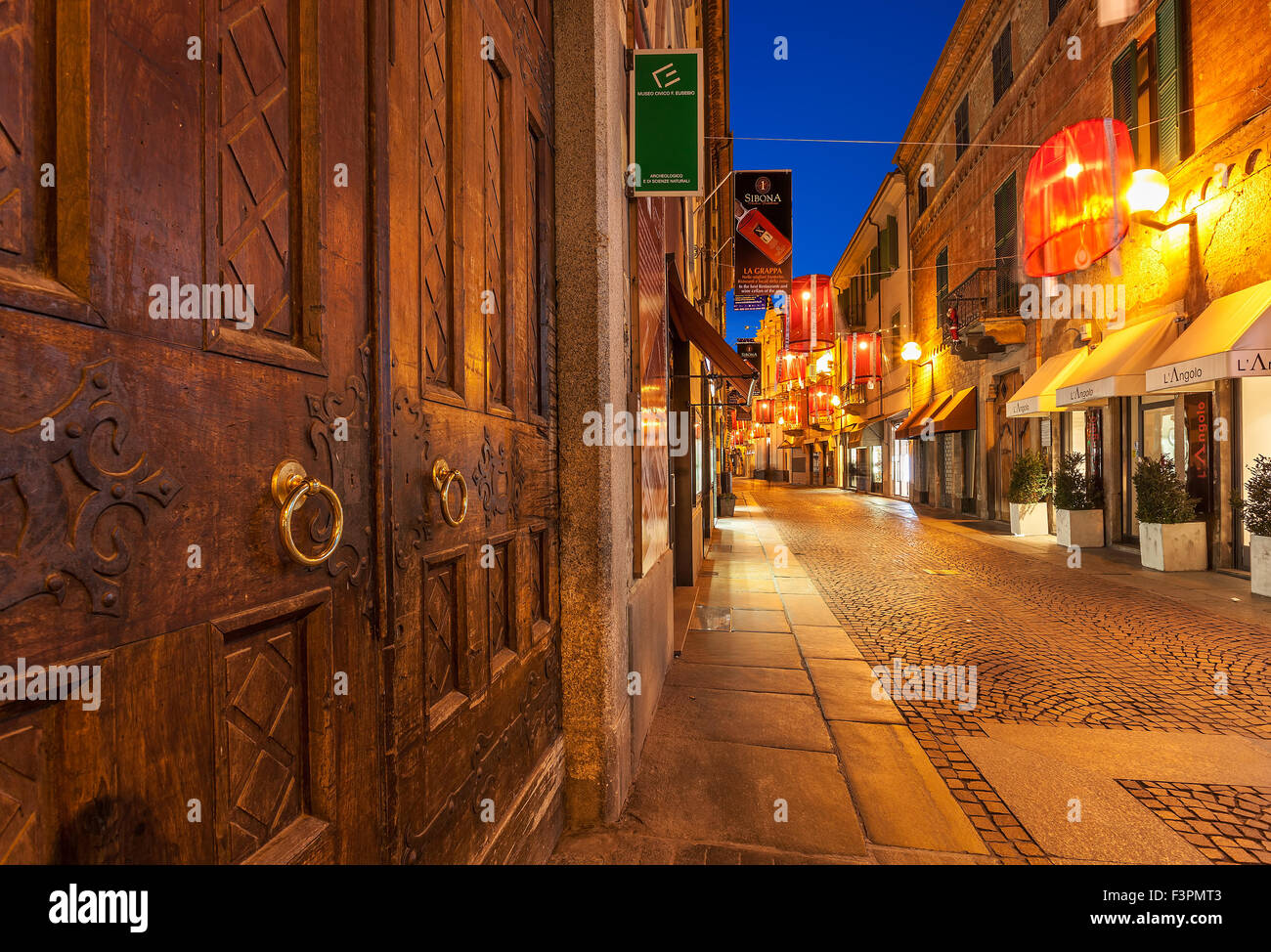 Old wooden door and pedestrian street with shops in old town of Alba, Italy. Stock Photo