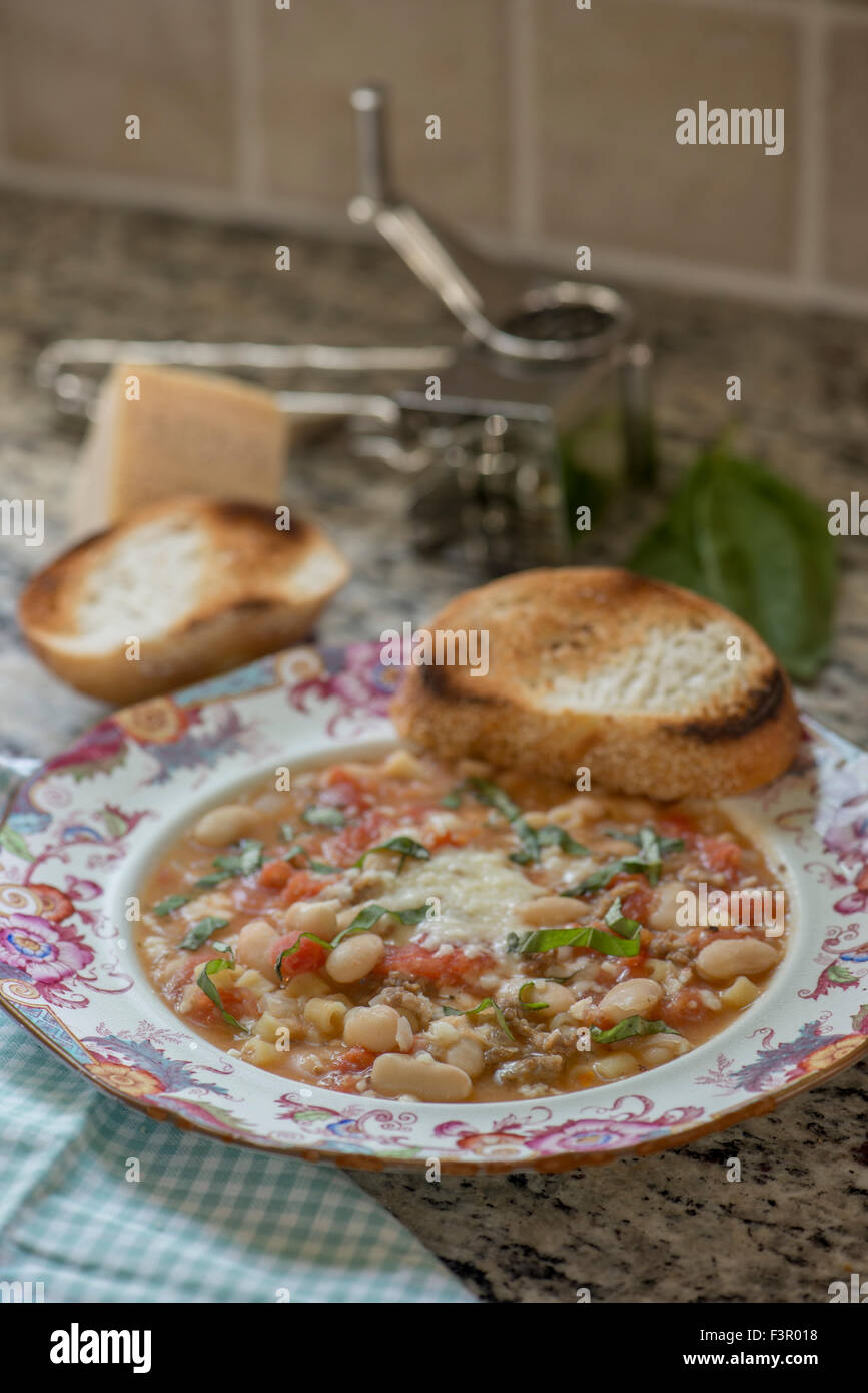 Pasta and Bean soup on kitchen counter, with toasted bread and a cheese grater. Stock Photo