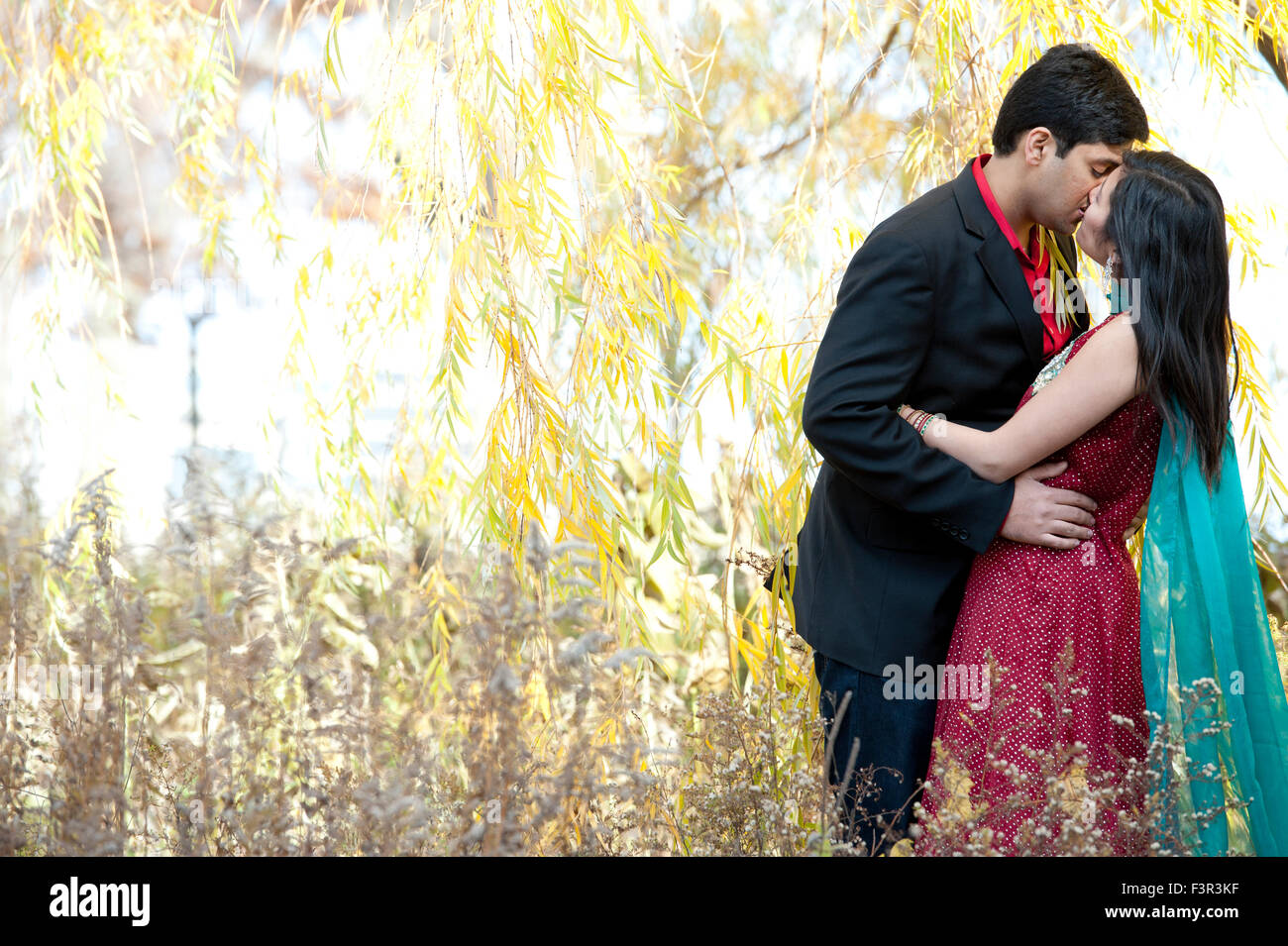 A young and happy Indian couple kissing under a willow tree in the Fall ...