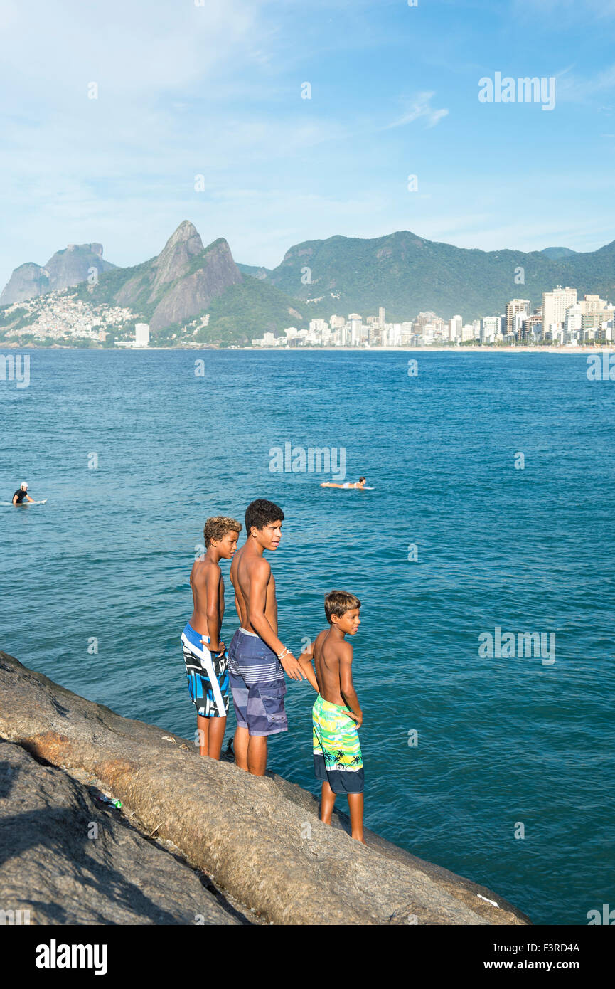 RIO DE JANEIRO, BRAZIL - FEBRUARY 03, 2014: Trio of young Brazilians stands ready to jump from the rocks at Arpoador in Ipanema. Stock Photo