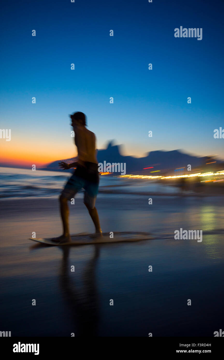 Action silhouette of Brazilian riding skimboard on Ipanema Beach Rio de Janeiro Brazil at sunset Stock Photo