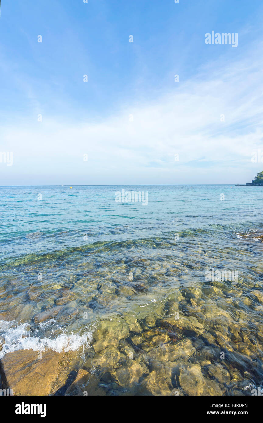 Rock beach with clear water and blue skies Stock Photo - Alamy