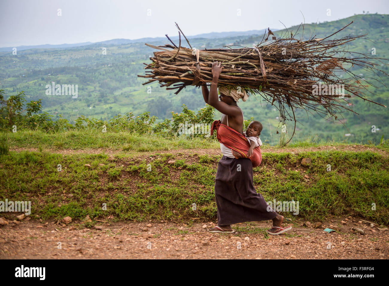 Woman with baby carries branches on head, Uganda, Africa Stock Photo