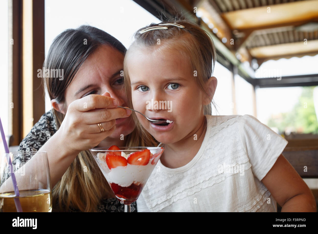 Mother feeds his daughter delicious sweet ice cream with strawberries in a restaurant. Shallow