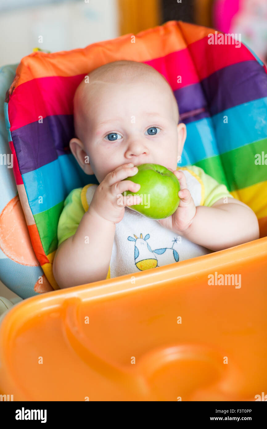 Adorable baby eating apple in high chair. Baby's first solid food Stock