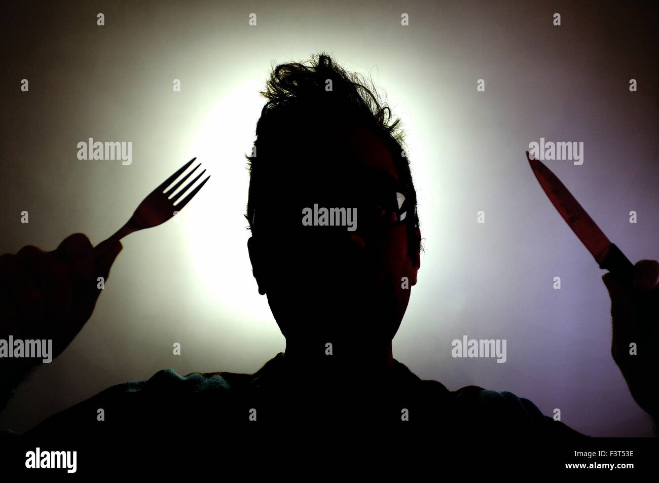 The silhouette of a man holding a knife and a fork. Stock Photo
