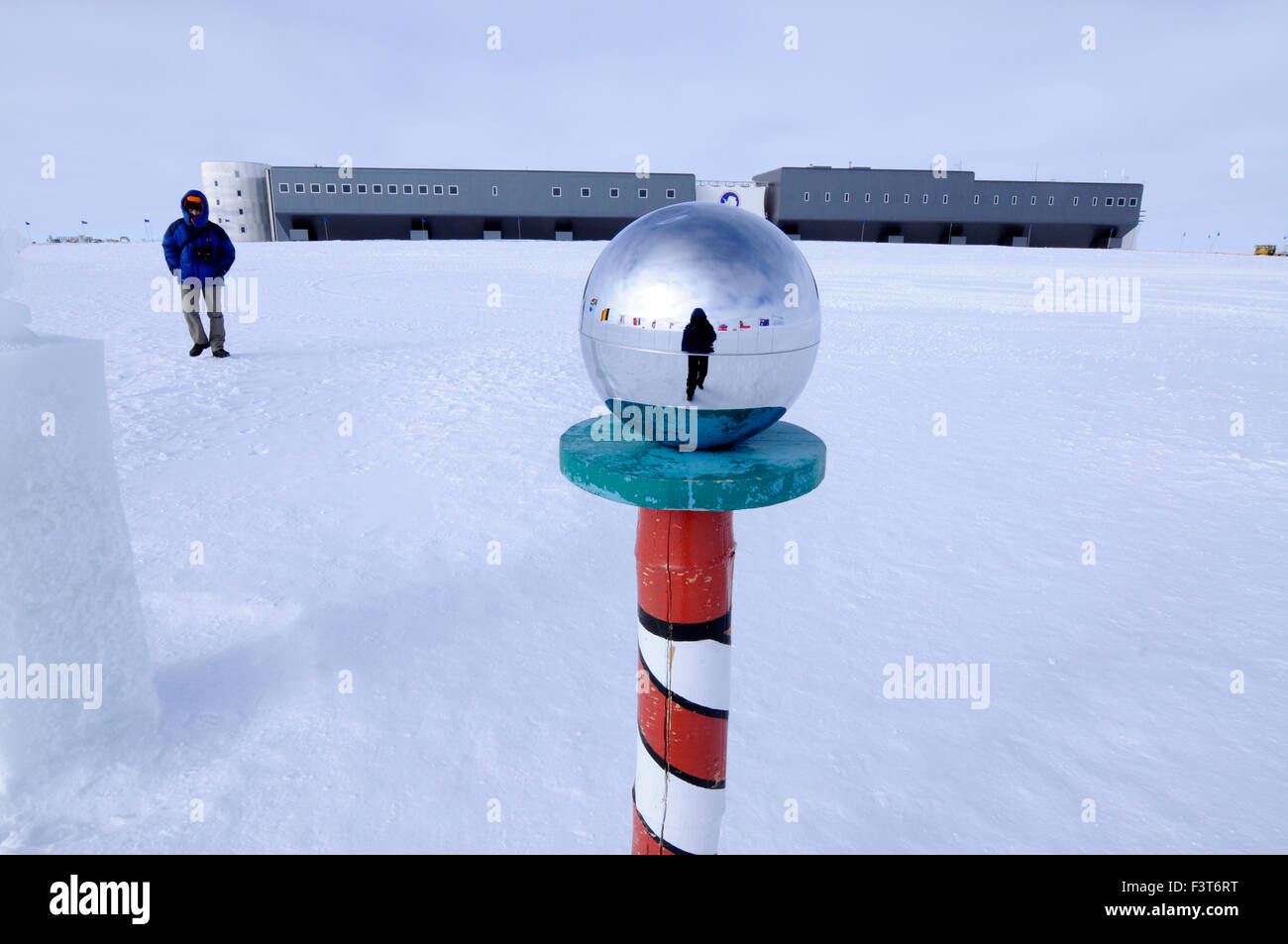 A scientist at the South Pole with Amundsen-Scott South Pole Station behind the mirror ball at the ceremonial pole Stock Photo