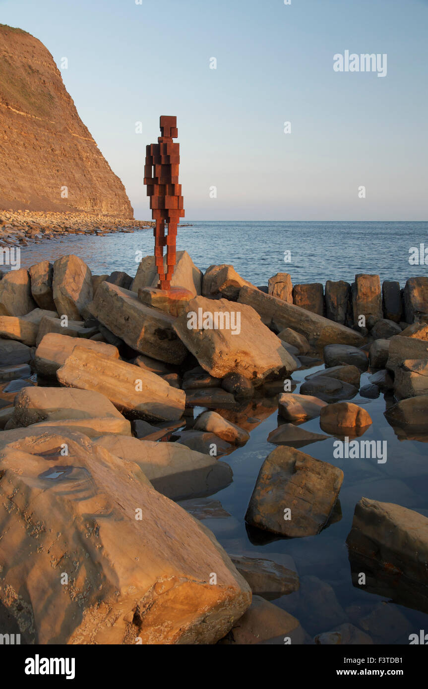 Antony Gormley’s life-sized iron sculpture of a human figure standing at the rocky waters edge at Kimmeridge Bay, Dorset, England, United Kingdom. Stock Photo