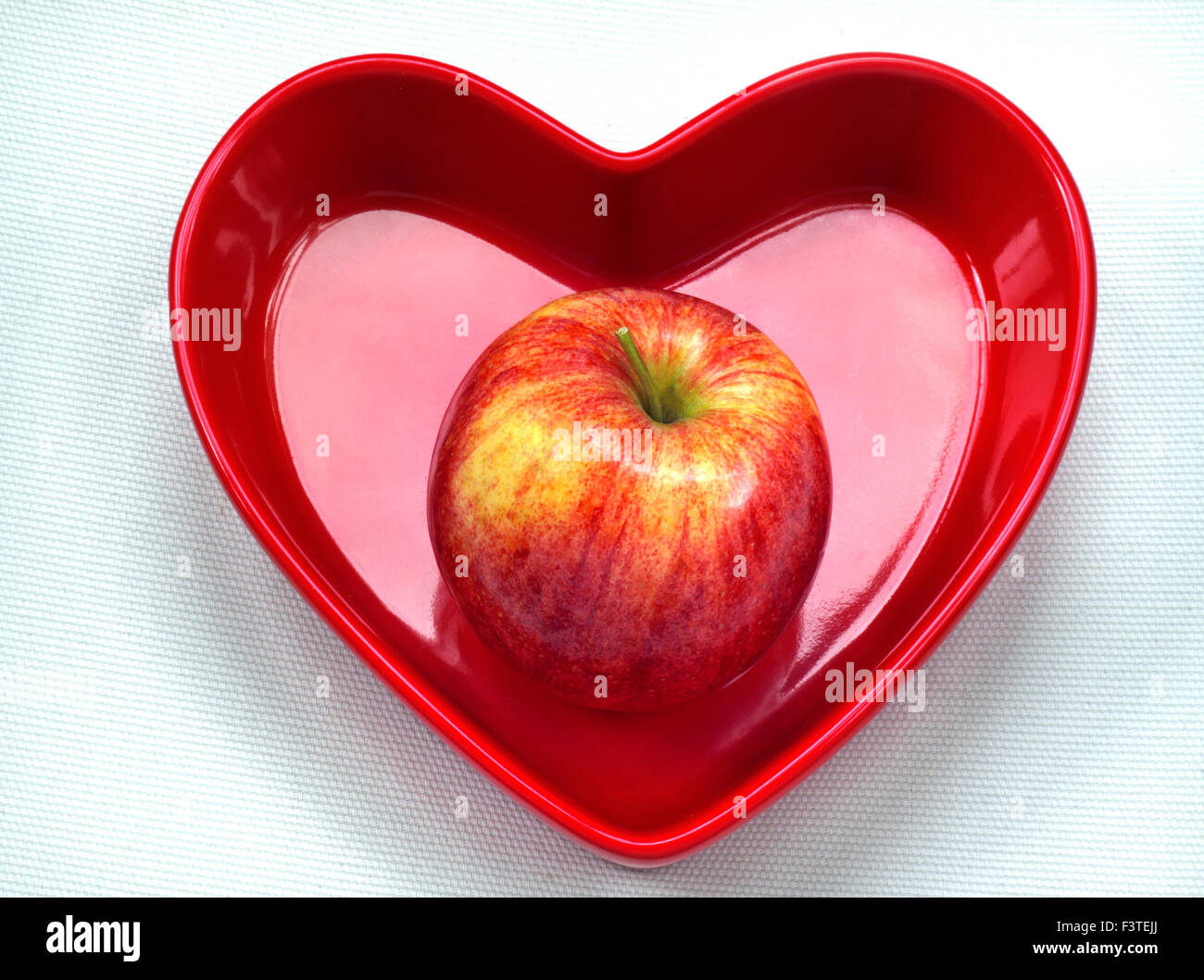 GALA APPLE HEART DISH Healthy eating concept / Perfect unmarked shiny sweet Gala Apple in red heart shaped dish on white background Stock Photo