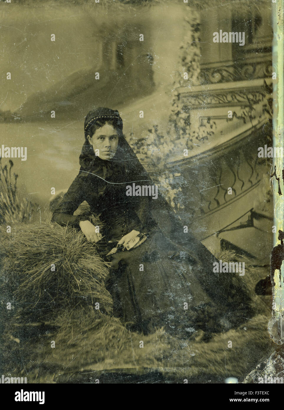 Woman in black dress sitting in front of painted background during a photo sitting that produced a tin-type photograph during the late 1800s in the United States of America. Stock Photo