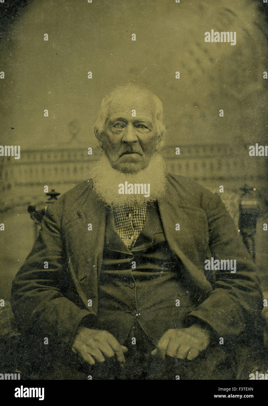 Older man with a white beard in suit seated in chair during a photo sitting that produced a tin-type photograph during the late 1800s in the United States of America. Stock Photo