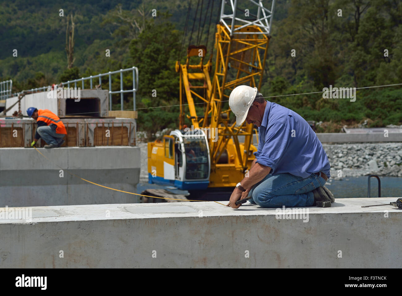 Builders construct a concrete bridge over a small river in Westland, New Zealand Stock Photo