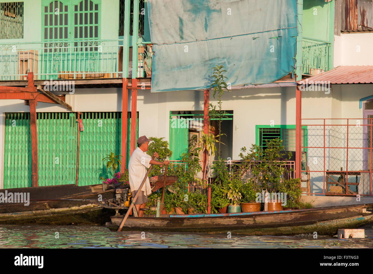 Vietnamese man rowing his timber boat past houses on the mekong river ...