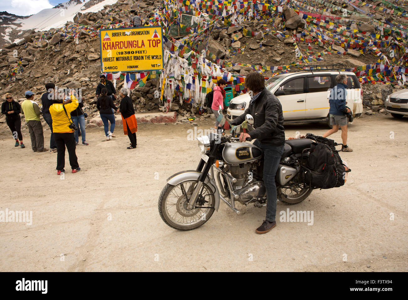 India, Jammu & Kashmir, Ladakh, Leh, Khardung La Pass top, motorcyclist watching pausing to watch, tourists at summit sign Stock Photo