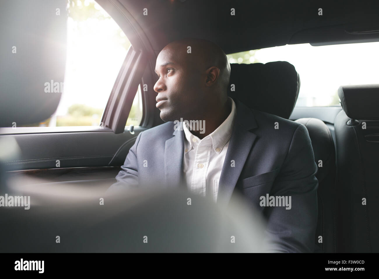 Young african businessman traveling to work in the luxury car on the back seat looking outside the window. Stock Photo