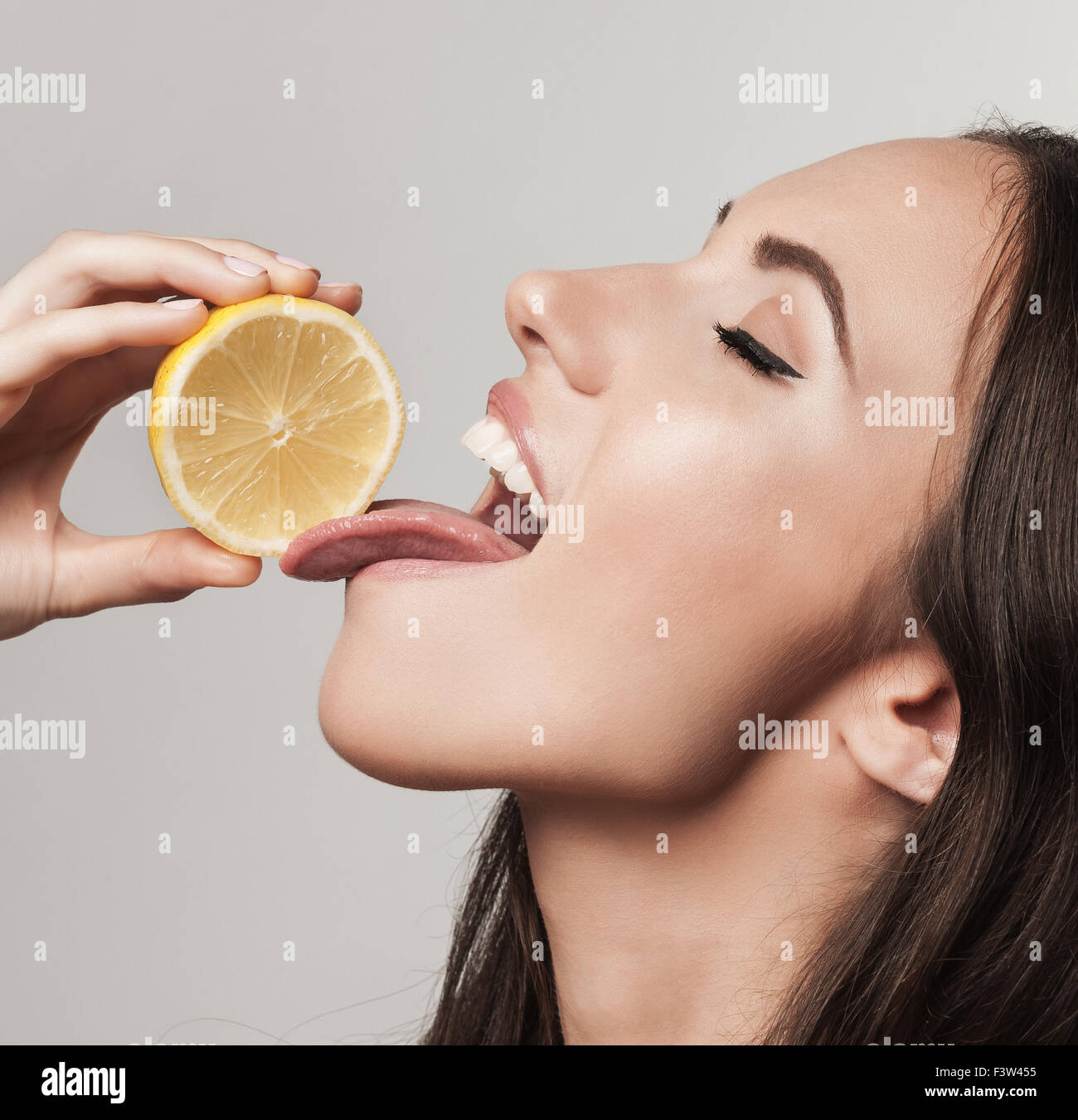 Portrait of woman promoting healthy eating. Beautiful young brunette woman holding fresh sliced lemon. Healthy eating lifestyle Stock Photo