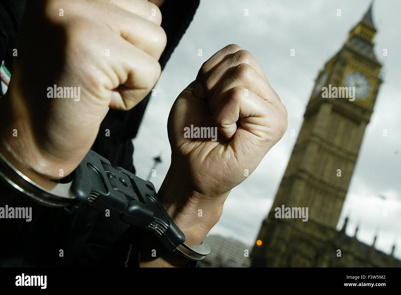 A man poses in front of the Houses of Parliament while wearing police handcuffs. Stock Photo