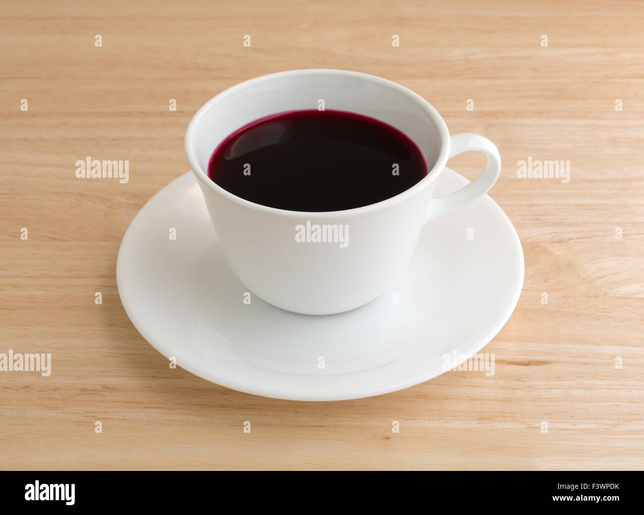 Beet juice in a white coffee cup and saucer atop a wood table top illuminated with natural light. Stock Photo