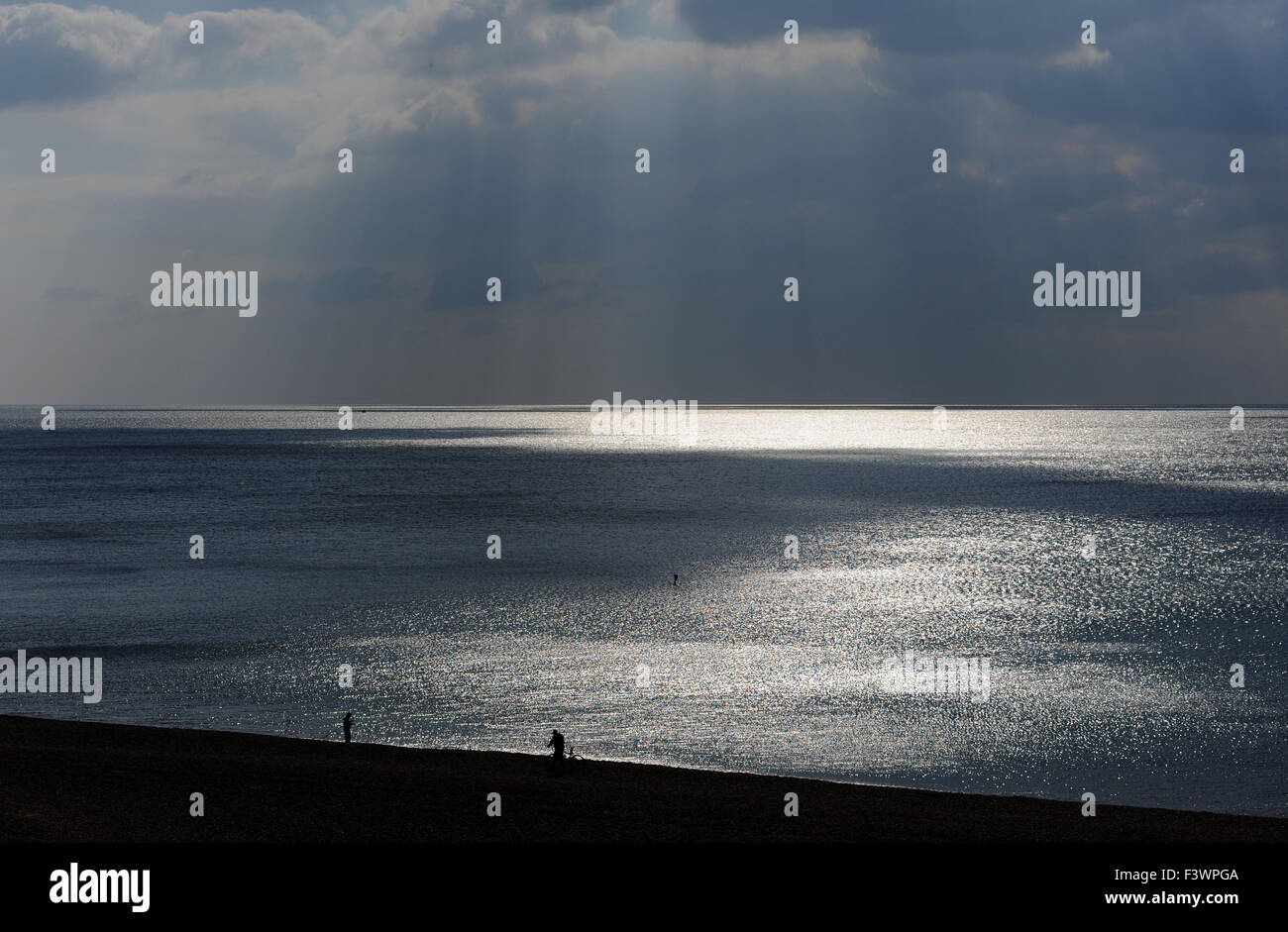 Brighton, UK. 13th October, 2015. A man pushes his bicycle along the beach as shafts of sunlight break through  the dark clouds which are forming off Brighton today The weather is set to become more unsettled over the next few days  Credit:  Simon Dack/Alamy Live News Stock Photo