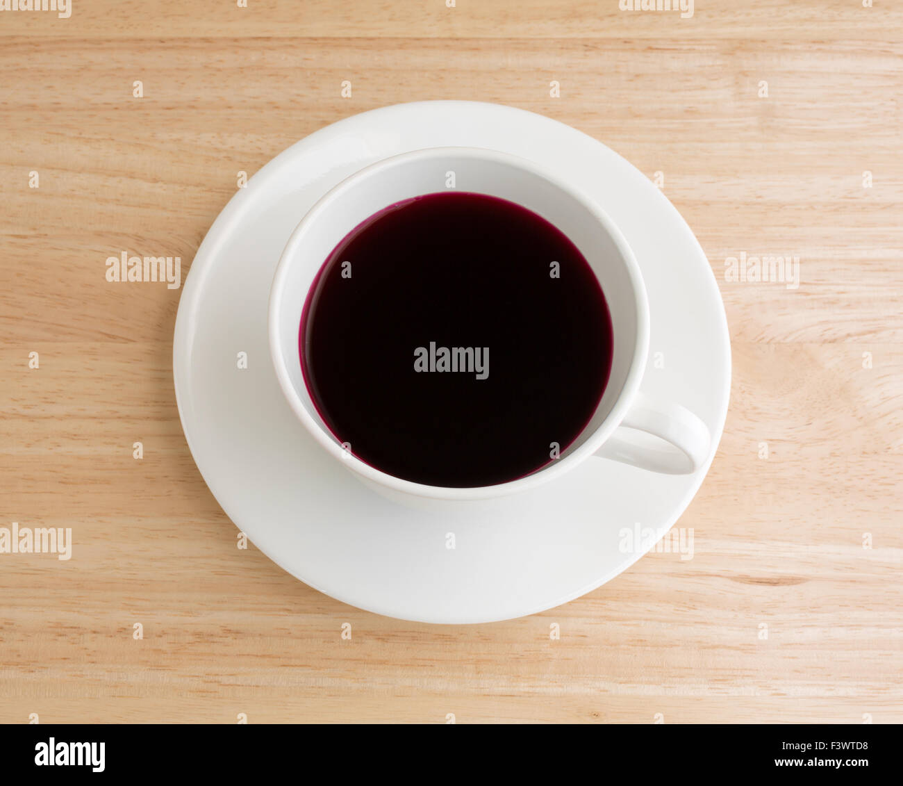 Beet juice in a white coffee cup and saucer atop a wood table top illuminated with natural light. Stock Photo