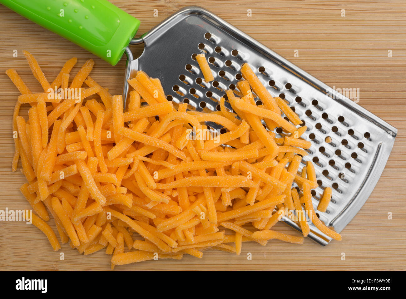 Close view of cheese that has been grated with a cheese grater atop a wood cutting board. Stock Photo