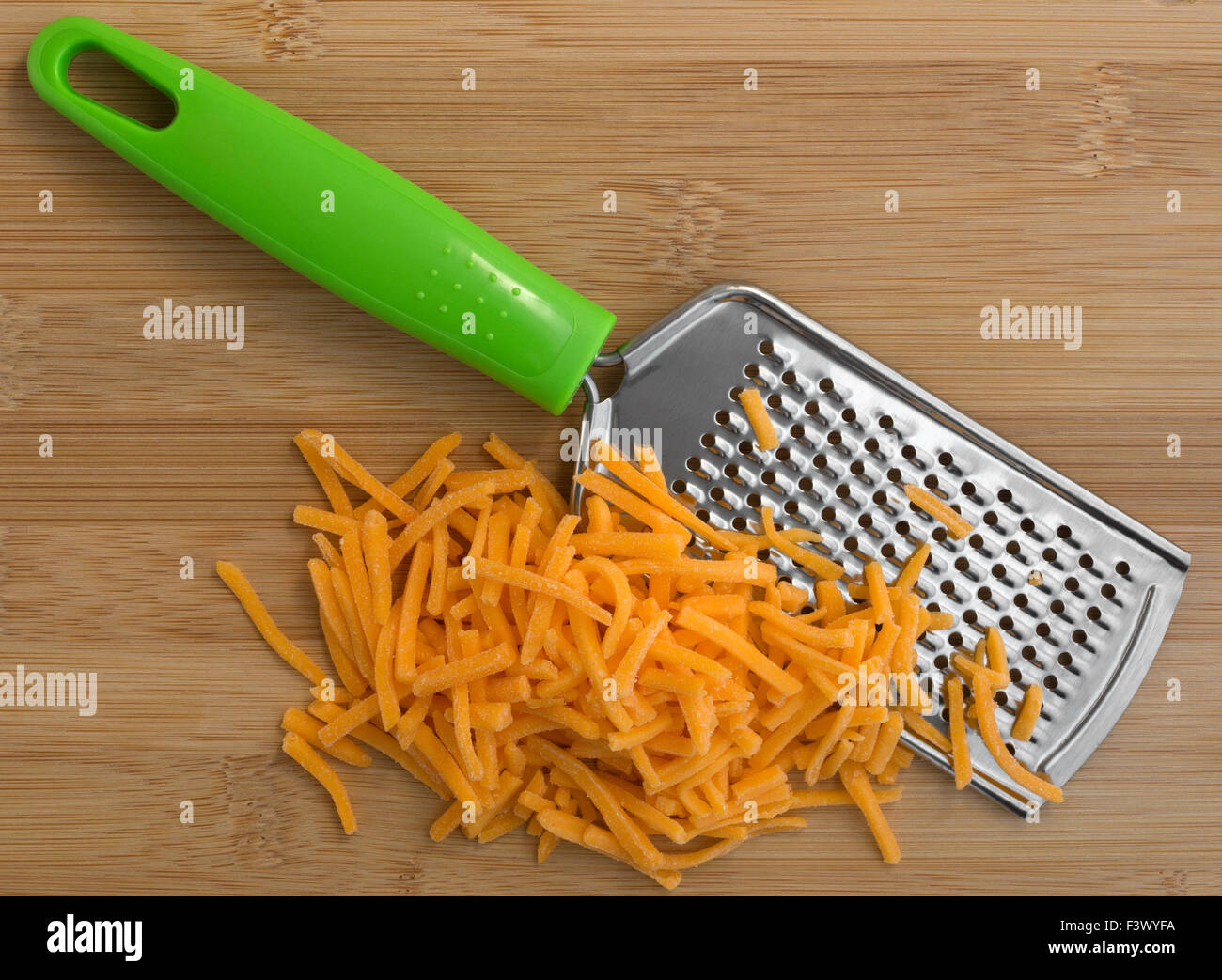 Top view of cheddar cheese that has been grated with a cheese grater atop a wood cutting board. Stock Photo