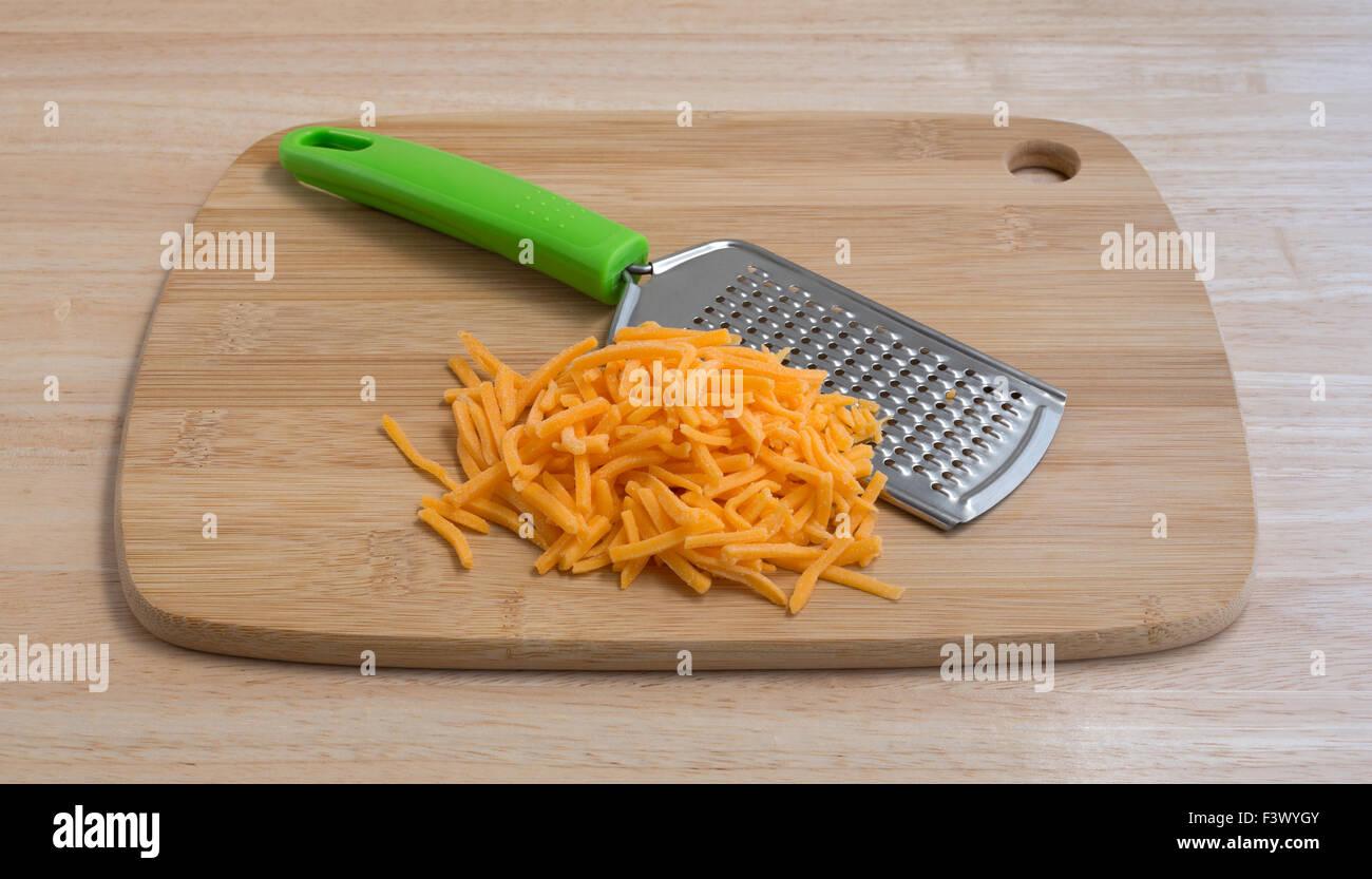 A portion of cheddar cheese that has been grated with a cheese grater atop a wood cutting board and counter top. Stock Photo