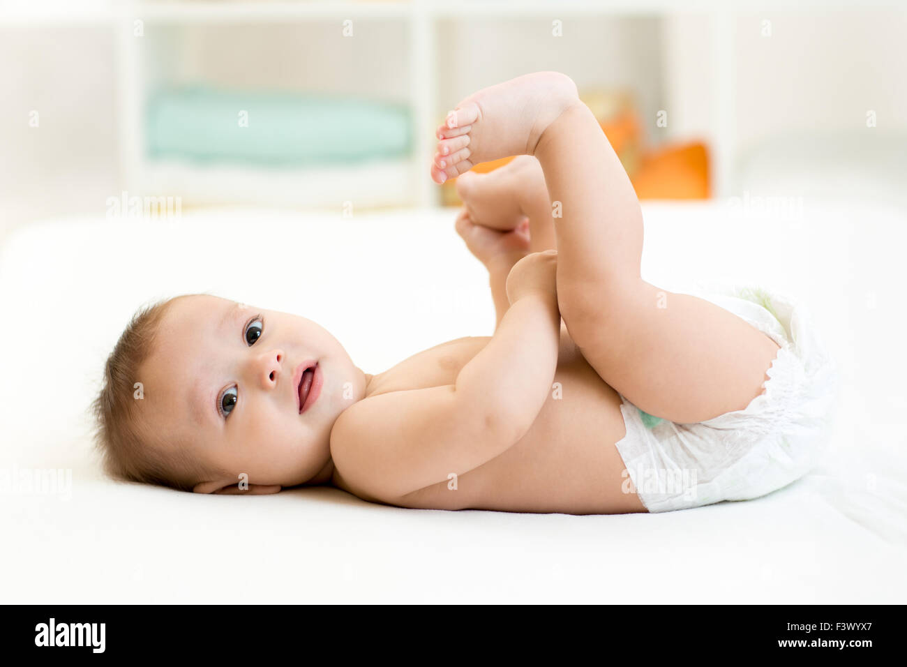 cute baby lying on white sheet and holding his legs Stock Photo