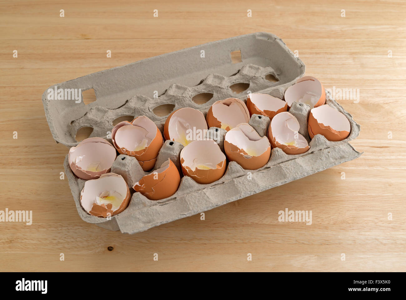 A dozen broken eggshells in an opened cardboard container on a wood counter top illuminated with natural light. Stock Photo