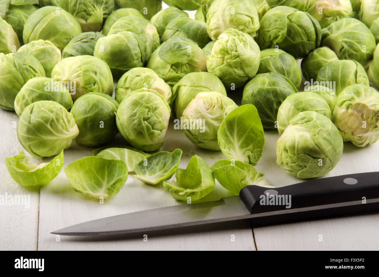 trimmed brussels sprouts and a kitchen knife on rustic table Stock Photo