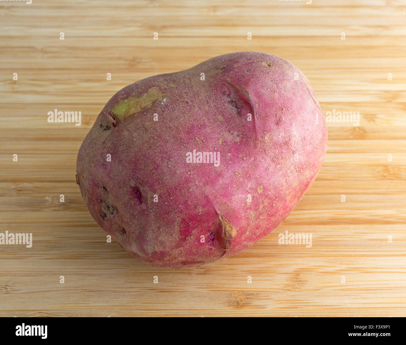 An organically grown red potato on a wood cutting board illuminated with natural light. Stock Photo