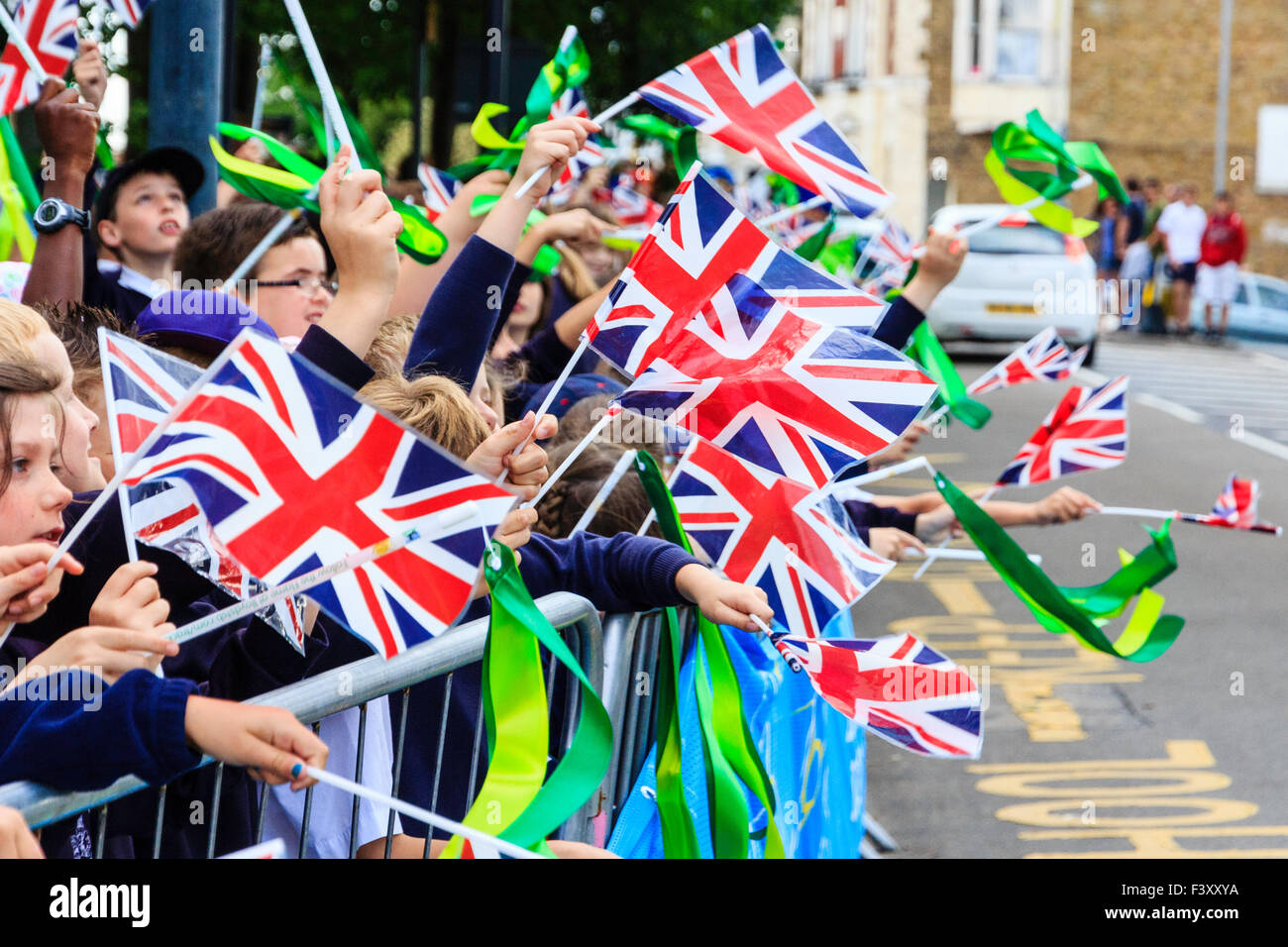 UK. 2012 Olympics. View along rows of school children, 7-9 year old. standing outdoors in front of street. Most holding flags, waving and cheering. Stock Photo