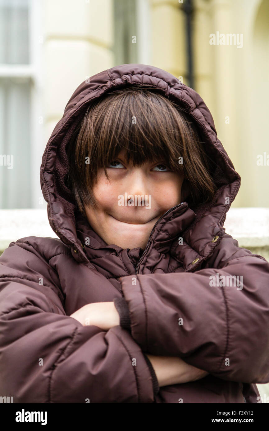Ten year old caucasian boy standing outside, cold, arms folded, in anorak, pulling comical face and smiling while looking upwards Stock Photo