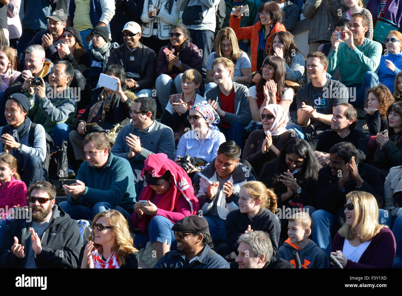 A large, diverse, all ages group of multi-ethnic people sitting outside on concrete bleachers reacting to watching street artists perform in the USA Stock Photo