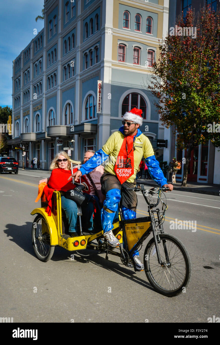Tourists celebrating the holidays enjoy a pedicab ride by a Santa hat wearing driver in the French Quarter in New Orleans, LA Stock Photo