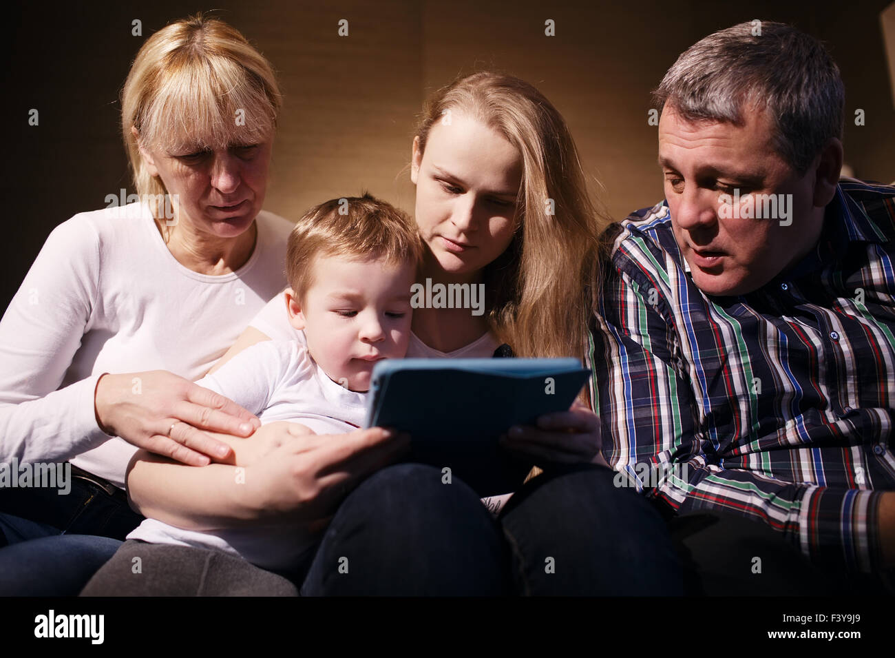 Family watching boy playing game on touchpad Stock Photo