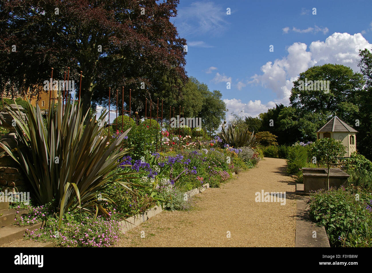 Gravel terrace lined with plants and shrubs with octagonal hut at the end; Belvoir Castle, UK Stock Photo