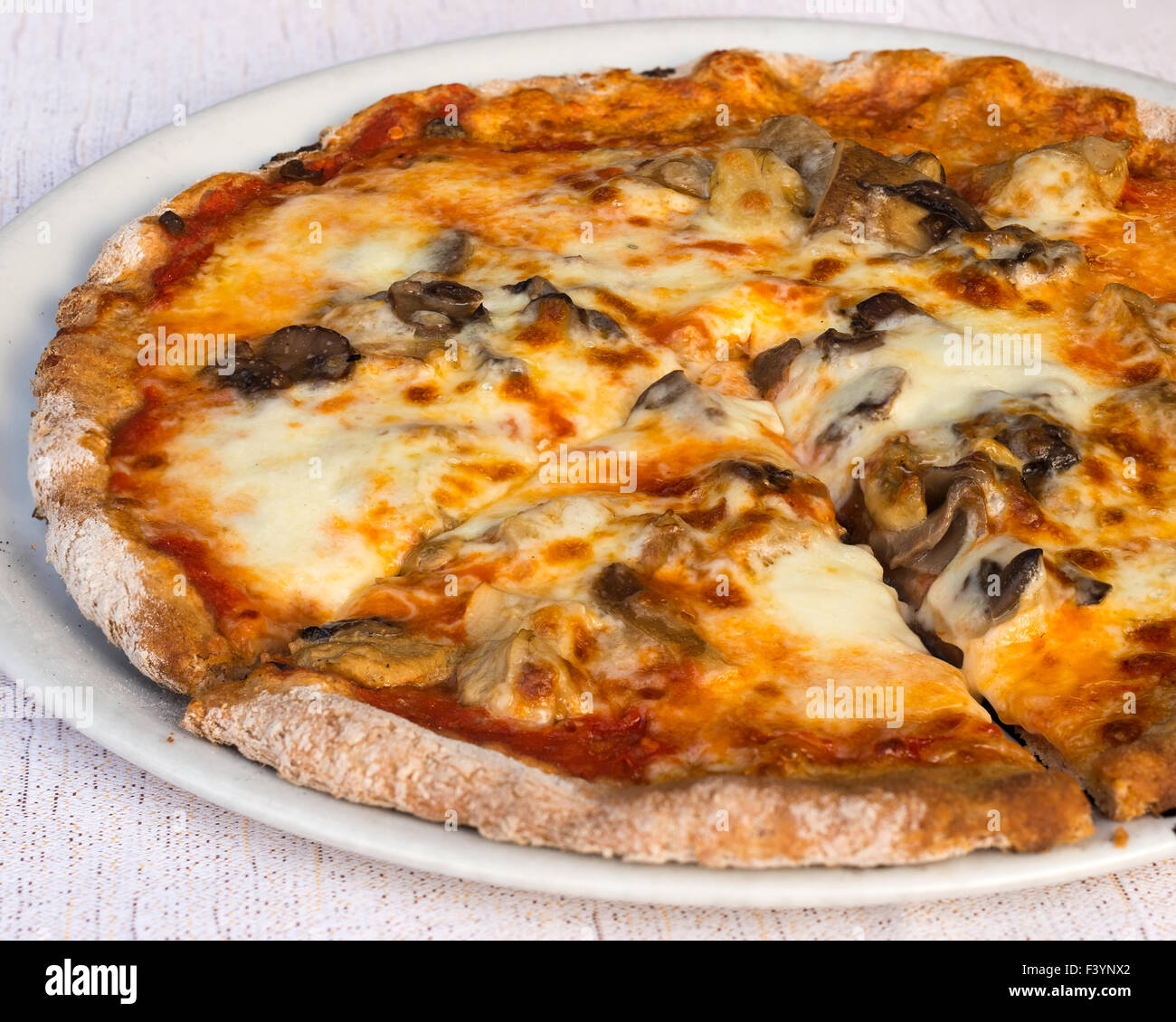 In the picture a slice of pizza with tomato, mozzarella cheese and mushrooms served on a white dish at the restaurant. Stock Photo