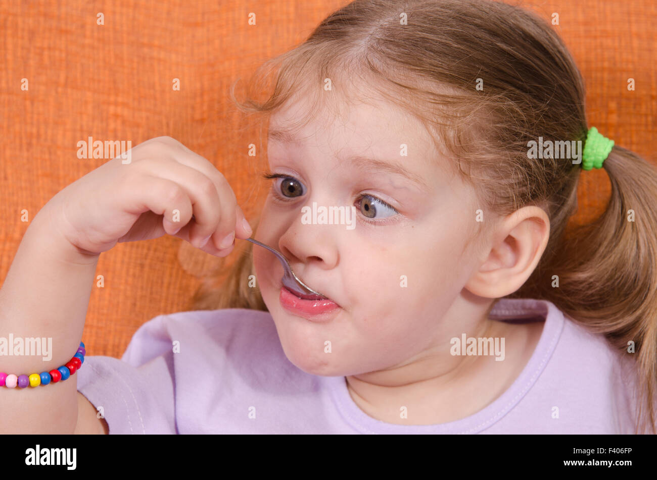 Funny girl squinted with his spoon in mouth Stock Photo