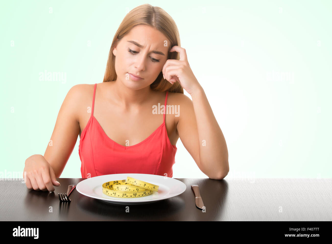 Concept image of a woman on a diet, eating a measuring tape in a green background Stock Photo