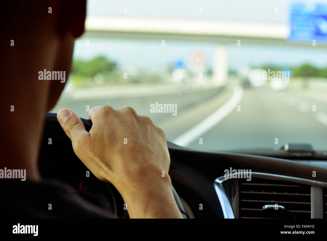 closeup of a young man, seen from behind, driving a car in a road with several lanes Stock Photo