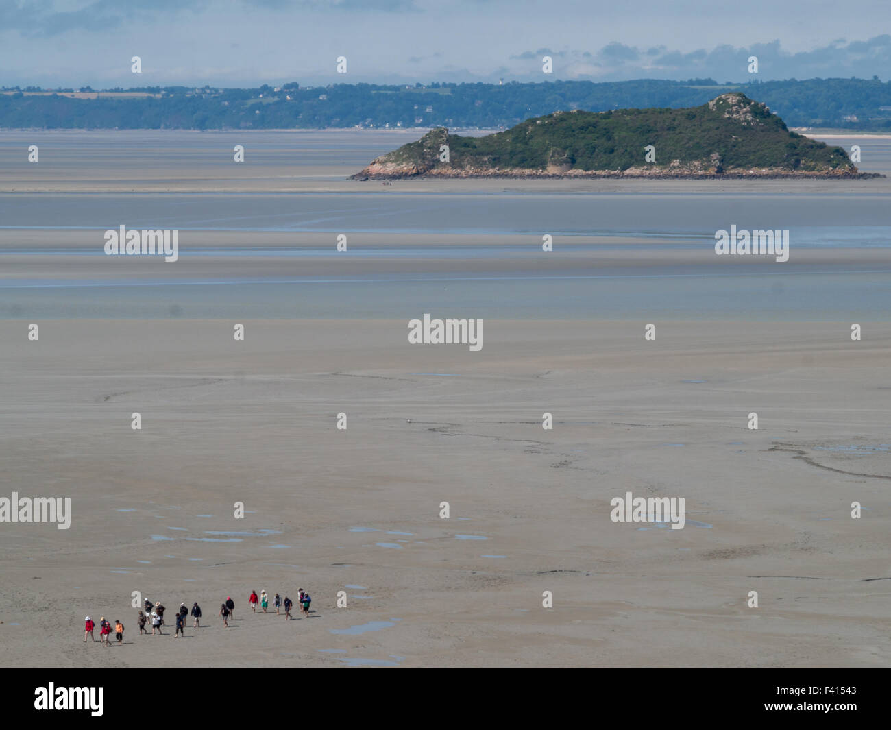 Group of tourists walking around Mont Saint-Michel in the low tide with an island in background Stock Photo