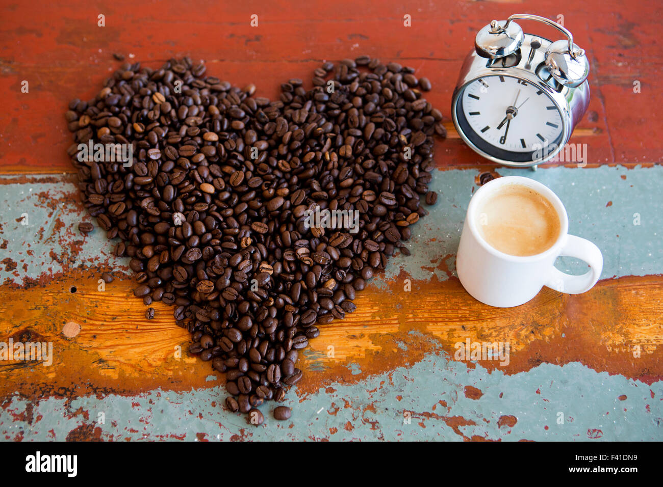 heart shape of coffee beans and cup of coffee and alarm clock on a vintage table Stock Photo