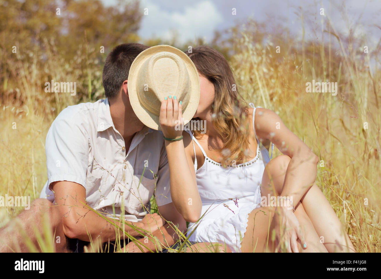 Couple kissing in the field behind a straw hat Stock Photo