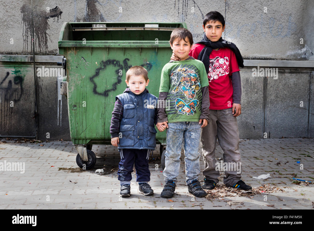 Three gipsy (roma) boys standing in front of a dumpster. Stock Photo