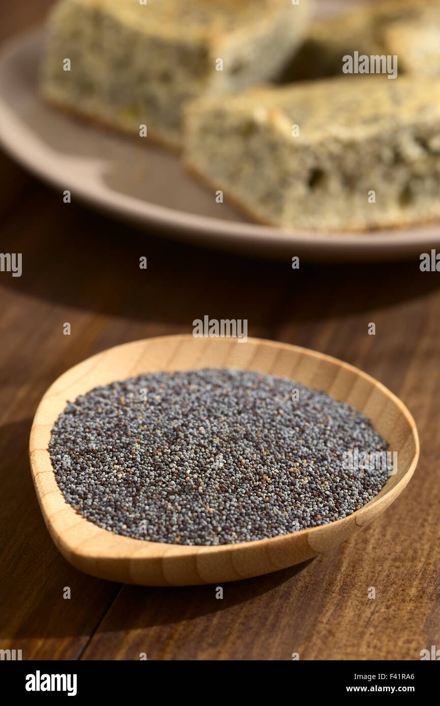 Raw poppy seeds on small wooden plate, poppy seed cake in the back ...